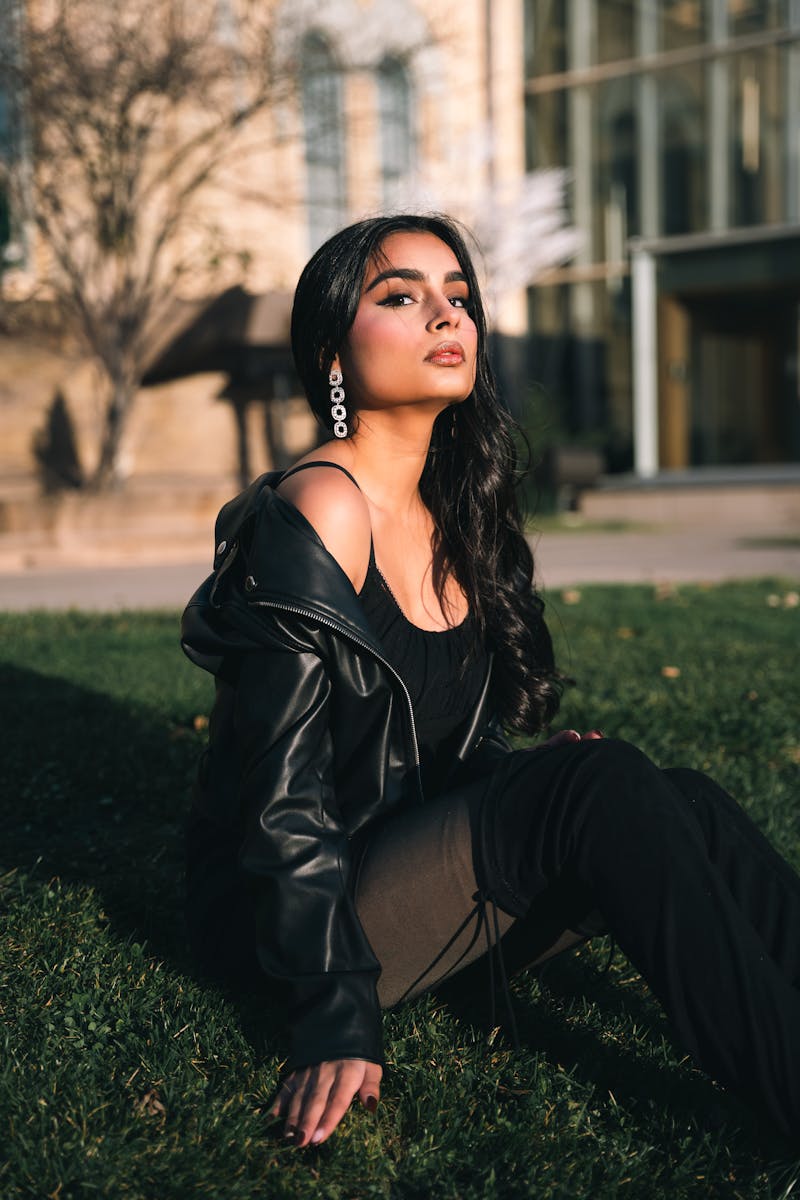 Fashionable woman sitting on grass in a black leather jacket and boots.